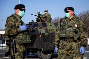 military personnel wearing facemasks with a tank in the background